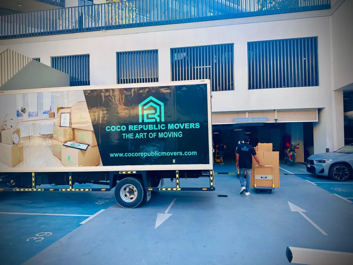 Mover wheeling cartons on a trolley from a moving truck in a Dubai building car park