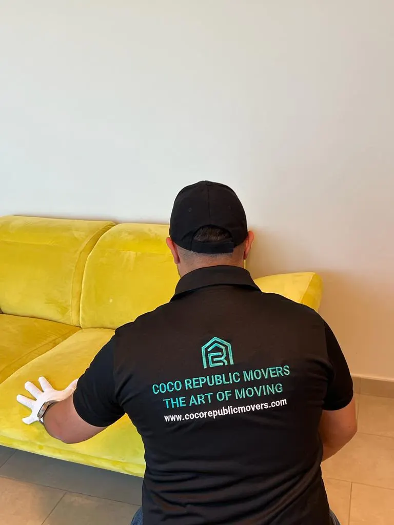 Mover in white gloves positioning a yellow velvet sofa in a Dubai apartment